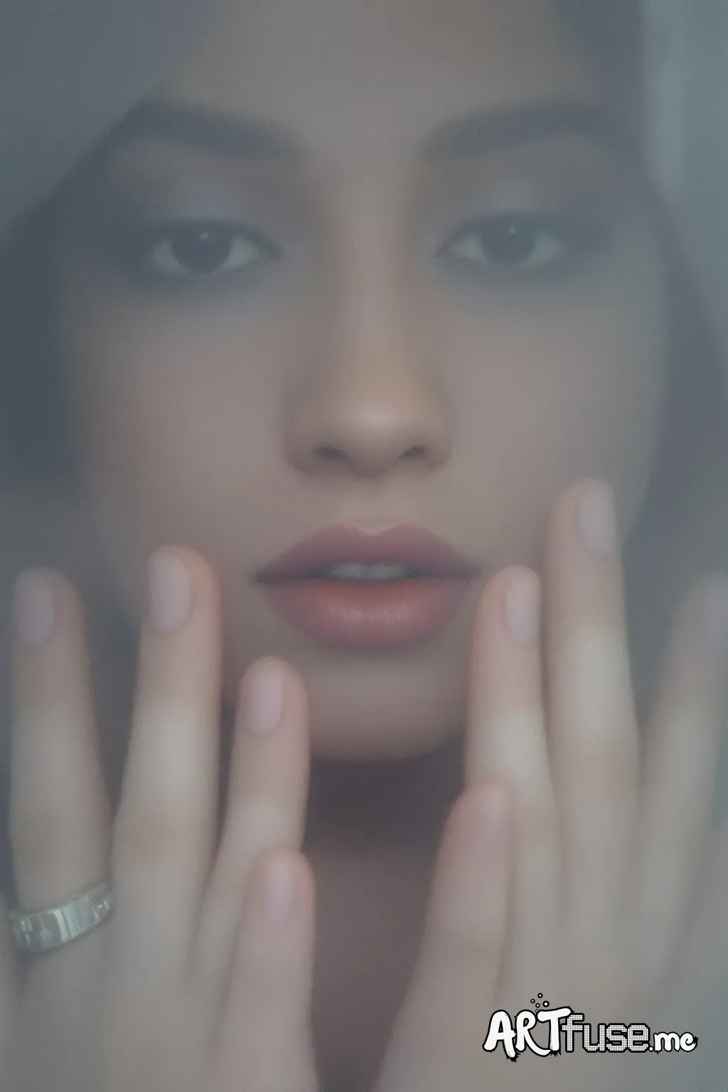 A close-up of a person's face pressed against a foggy, semi-transparent surface, creating a blurred, ethereal effect. The person's lips are slightly parted, and their nose and part of their face are visible through the frosted glass. Their hands are placed on the surface with fingers spread apart, adding a sense of longing or contemplation. The image has a soft, muted color palette with subtle lighting, giving it a dreamy, abstract feel. Small water droplets are scattered on the surface, enhanci